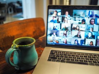 A photo of a blurry zoom screen on a laptop setting on a table with a coffee cup in the foreground.