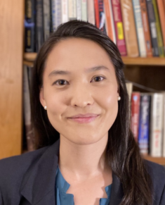 Ellen Meiser looks into the camera with a smile, standing in front of a bookshelf.